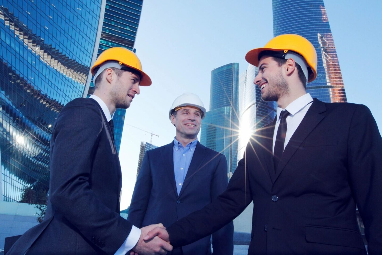 Three men in suits and hard hats shaking hands.