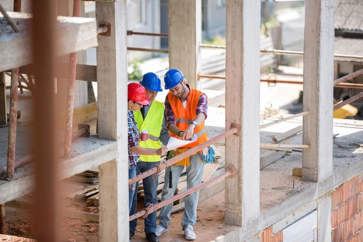 Two men in hard hats and safety vests looking at a building plan.