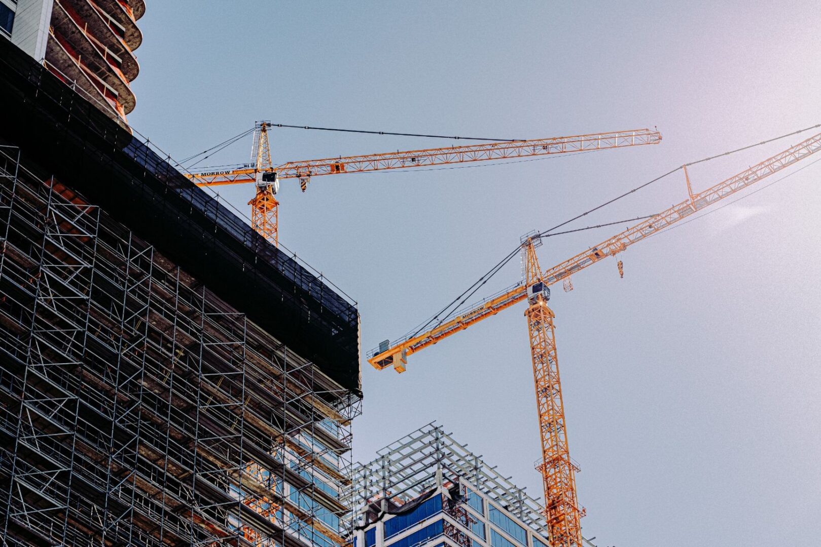 Two cranes are in the sky next to a building.