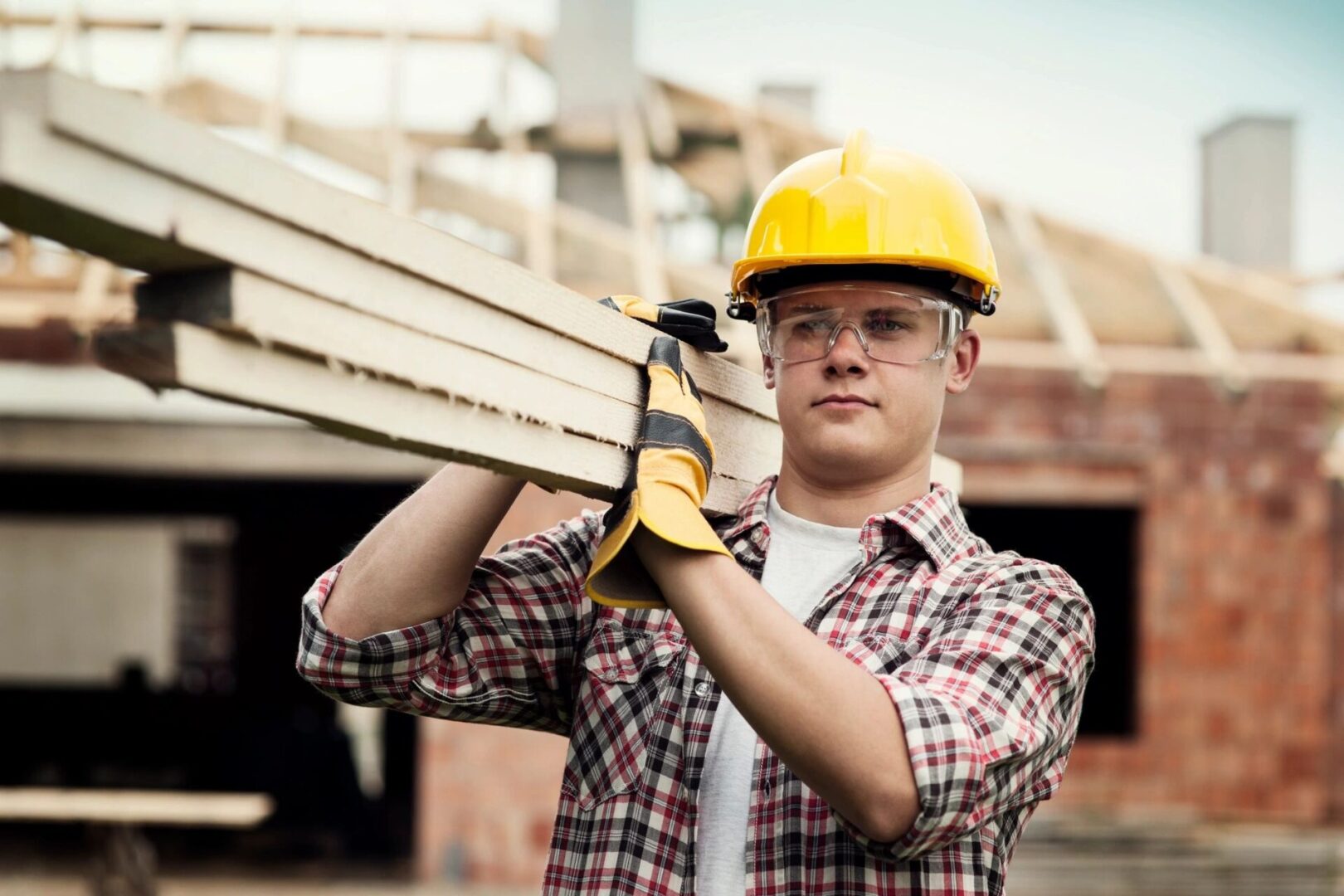 A man in yellow hard hat holding wood.