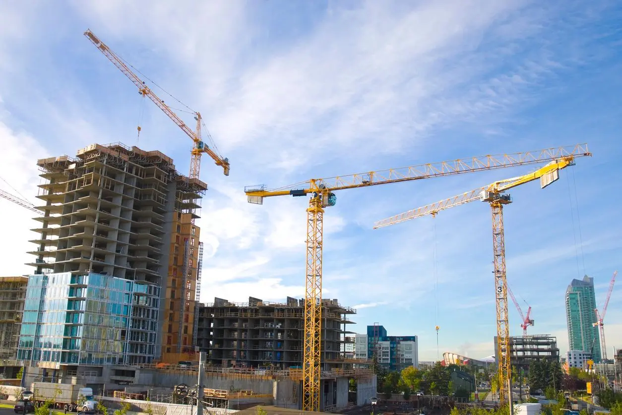 A group of cranes in front of some buildings.