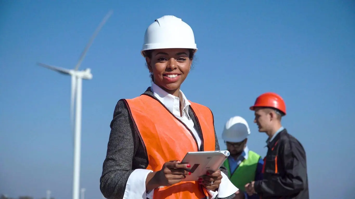 A woman in an orange vest holding a tablet.